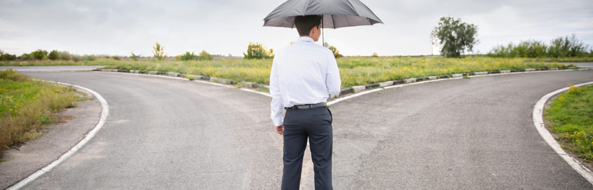 Businessman With Umbrella Standing At Crossroads. Concept Of Choice