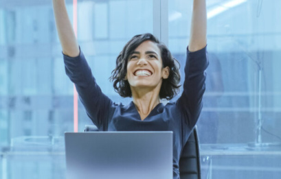 Shot Of The Beautiful Businesswoman Sitting At Her Office Desk, Raising Her Arms In A Celebration Of A Successful Job Promotion.