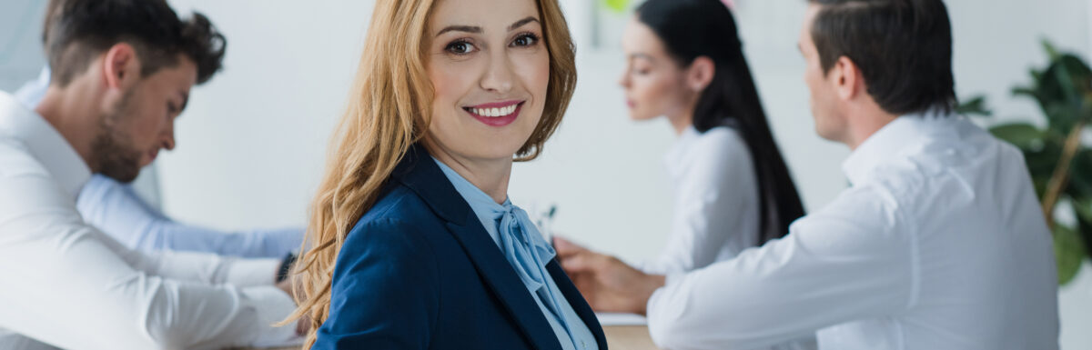 Selective Focus Of Smiling Businesswoman And Colleagues At Workplace In Office